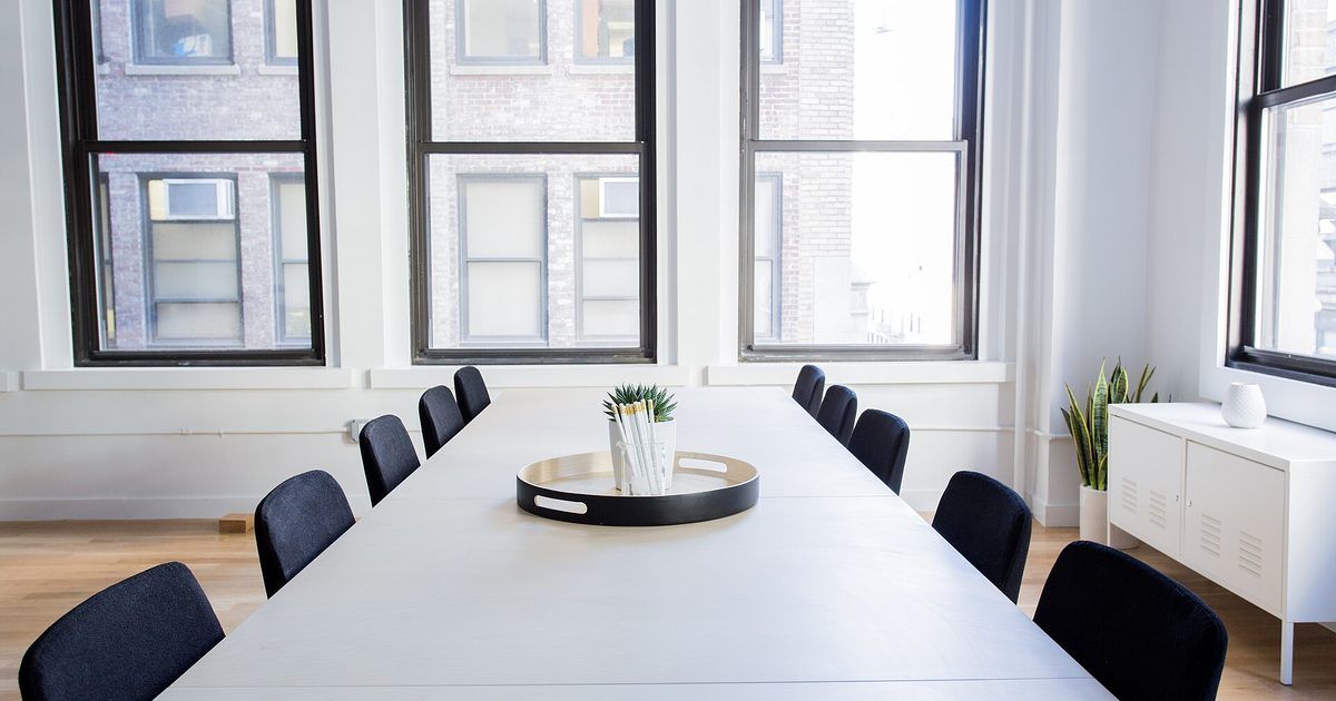 Mesa de reuniones blanca con sillas negras a ambos lados, frente a ventanas