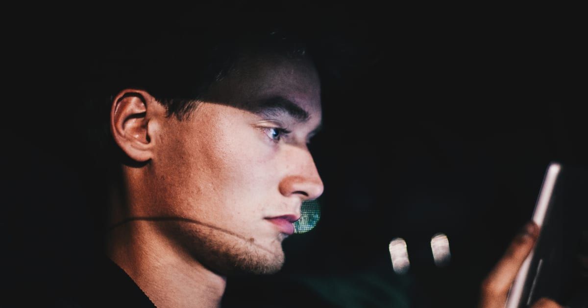 Hombre de perfil en la oscuridad, con el rostro iluminado por la pantalla del teléfono que sostiene en la mano