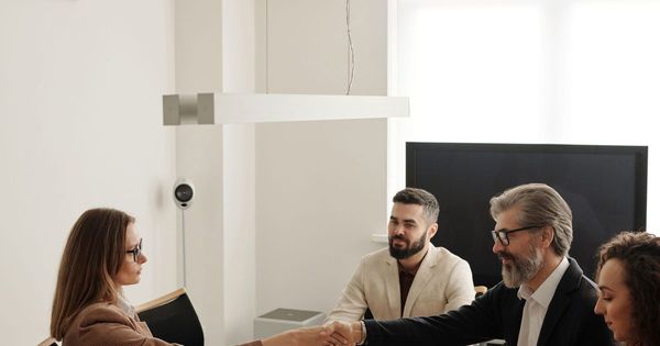 Cuatro personas en una mesa de reuniones, dos de ellas se dan la mano