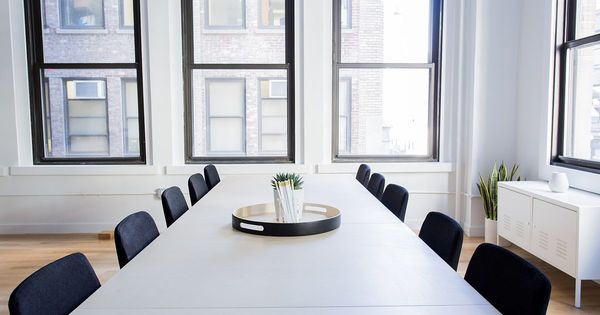 Mesa de reuniones blanca con sillas negras a ambos lados, frente a ventanas