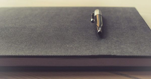 Bolígrafo metálico sobre un cuaderno de tapa gris, sobre una mesa de madera